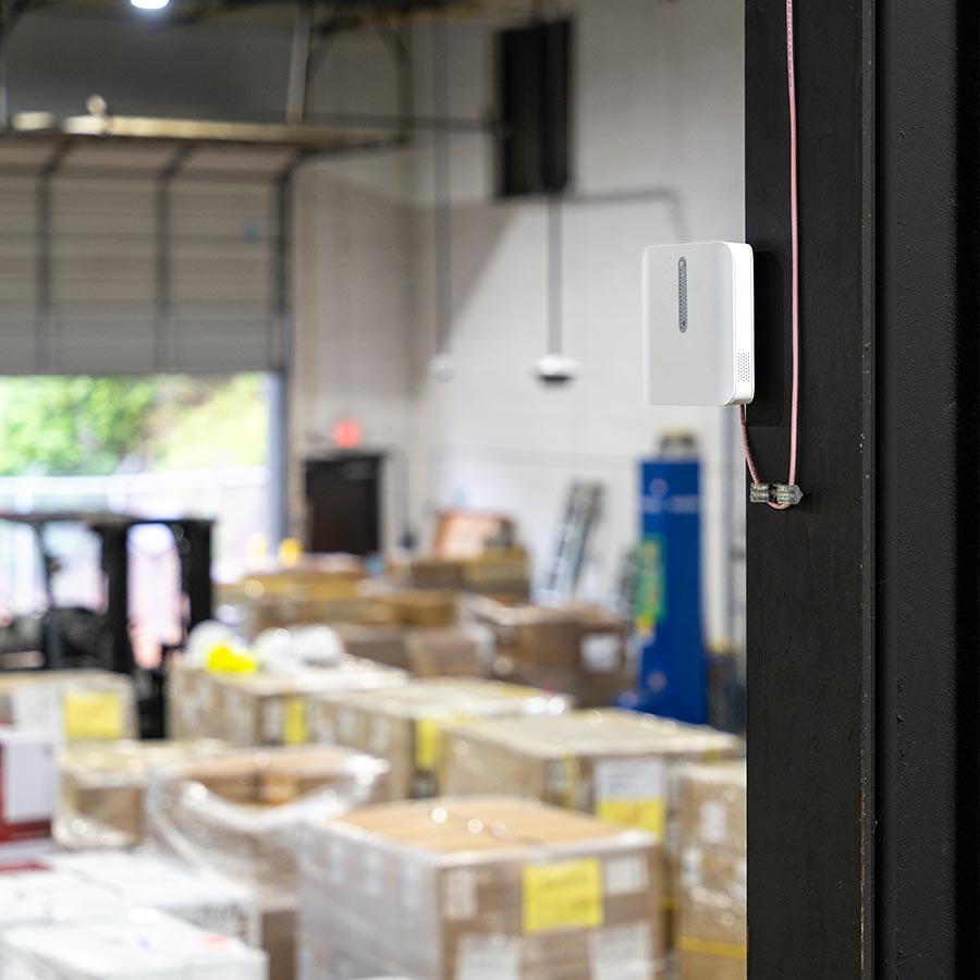 White environmental sensor mounted on a beam in a warehouse