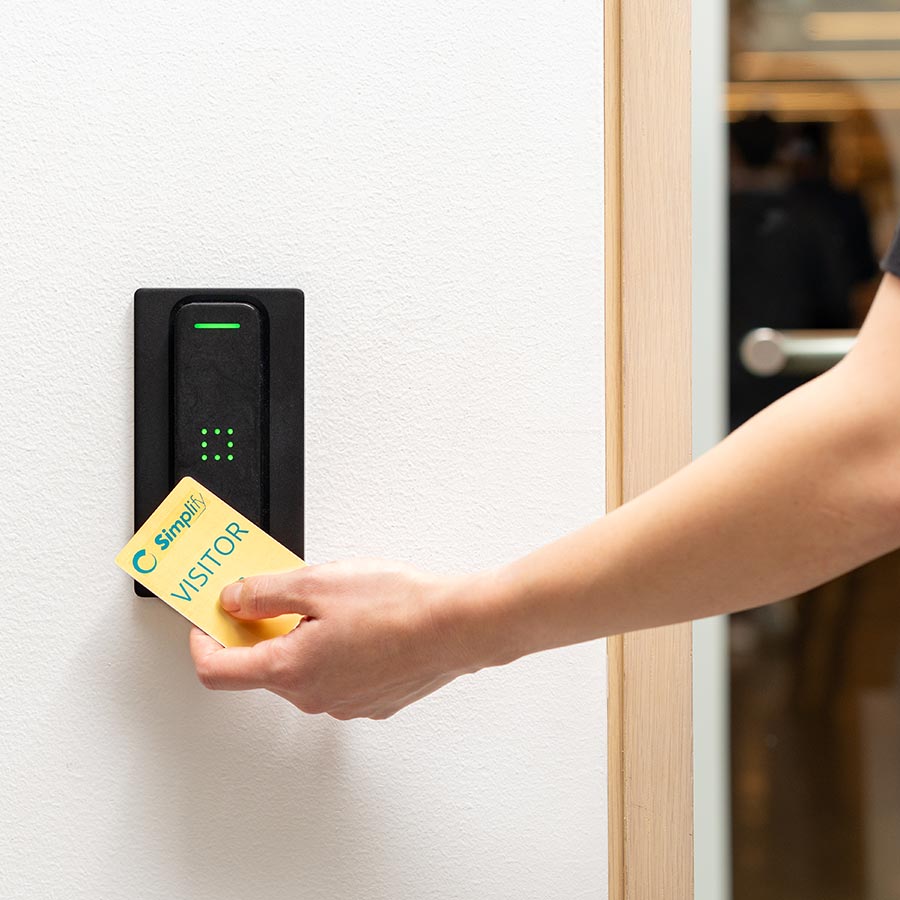 Hand holding a yellow visitor badge to a black card reader